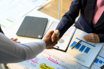 Business people shaking hands over business plan and financial charts