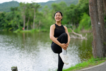 Young Asian sportswoman stretching legs by the lake in a public park
