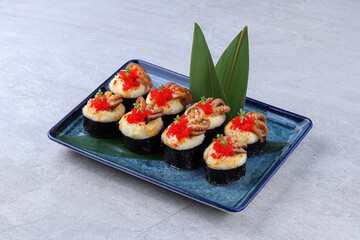 Elegant sushi platter with octopus, fish roe, and herbs on seaweed-wrapped rice, served on a blue ceramic plate with green leaves