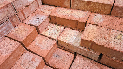 Fototapeta premium Close-up view of a stack of reddish-brown bricks. The bricks show some surface imperfections and slight variations in color. They are arranged in an overlapping pattern.