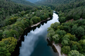 A serene river meanders through a lush green forest, reflecting the vibrant hues of nature under a calm sky, creating a peaceful and picturesque scene for outdoor enthusiasts.