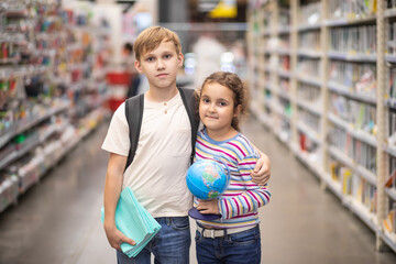 Cute little girl and teenager boy choosing school stationery in supermarket