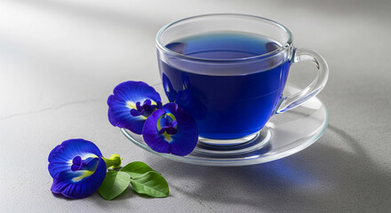 A teacup of vibrant blue butterfly pea flower tea with fresh flowers on a saucer. This image represents herbal wellness, a healthy lifestyle, and natural, exotic drinks.