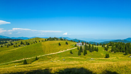 Aerial panoramic view of Velika Planina in Slovenia featuring vast green alpine pastures dotted with traditional mountain huts, set against the stunning backdrop of the Kamnik-Savinja Alps