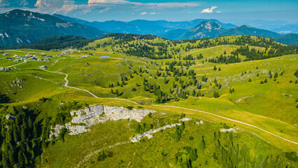 Aerial panoramic view of Velika Planina in Slovenia featuring vast green alpine pastures dotted with traditional mountain huts, set against the stunning backdrop of the Kamnik-Savinja Alps © Viktor
