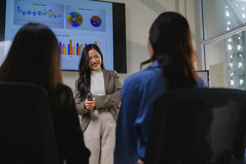 Businesswoman holding microphone presenting business plan to colleagues in meeting room