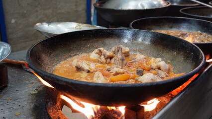 Chicken karahi simmering in a large wok over an open flame, street food