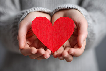 Fototapeta premium Heartfelt tenderness as woman gently holds a vibrant red heart in her hands, radiating love, care, and compassion for a truly heartwarming moment