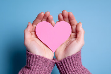 Fototapeta premium Woman's gentle hands tenderly hold a pink heart shape, radiating love and care – perfect for Valentine's Day promotions and heartfelt messages