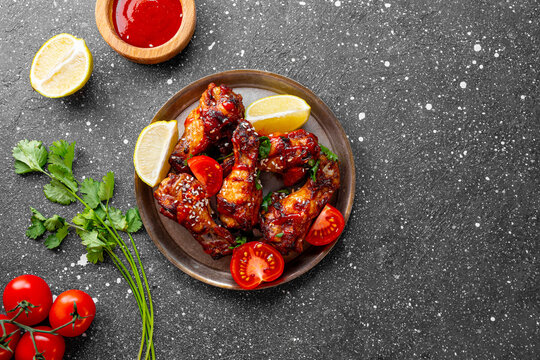 Spicy chicken wings with sriracha sauce and lime in a plate on dark background top view