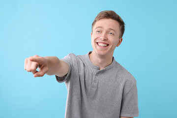 Handsome man laughing and pointing at something on light blue background. Positive emotion