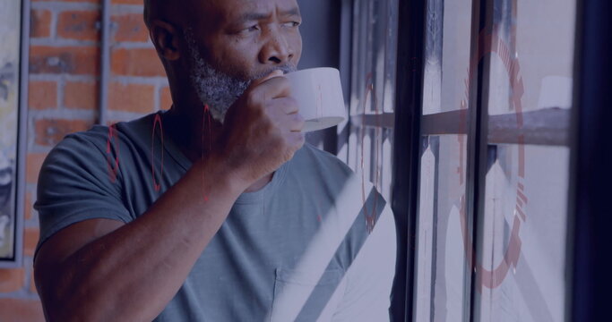 Sipping beverage, mature man wearing grey t-shirt in loft, holding white mug near multi-pane window