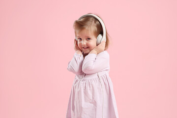 Cute little girl in headphones on pink background