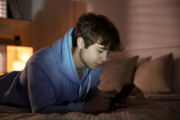 Obraz premium Teenage boy using smartphone on bed at home