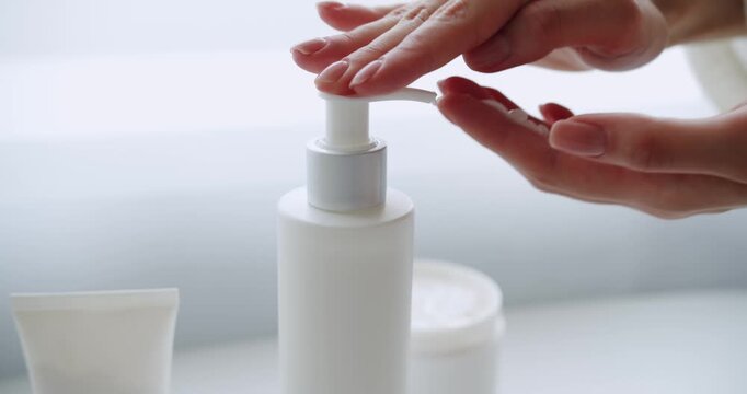 Finger push button on cream bottle in clean hand on white room background. Close up. Washing at bathroom, Woman hands pushing pump plastic lotion bottle applying moisturizing cream on hands.