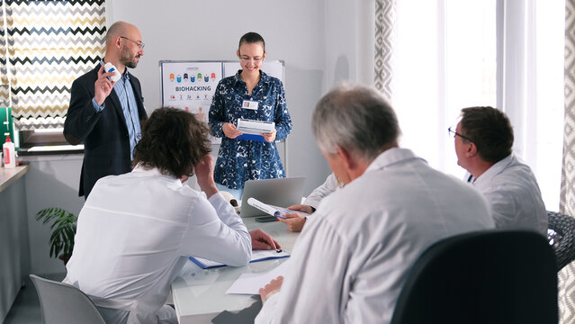 A happy man and a woman present to a group of doctors a new development by scientists - flu pills. A group of doctors attentively listens to the presentation