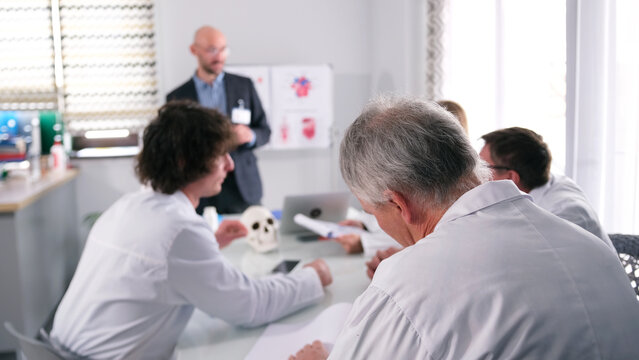 Several doctors are sitting at a table in a conference room and listening to a sales representative's presentation. Briefing at the clinic