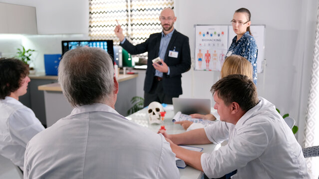 A group of people listens to two lecturers at a presentation on biohacking. There are several doctors sitting at a table in the conference room