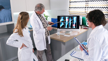 Obraz premium The surgeon discusses the patient's case with the interns. A group of doctors looks at a computer monitor that displays X-rays