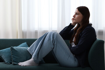 Sad young woman sitting on sofa at home