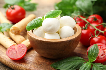 Tasty mozzarella cheese balls, tomatoes, basil and grissini on table, closeup
