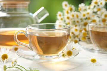 Aromatic tea in glass cups and chamomile flowers on white wooden table, closeup