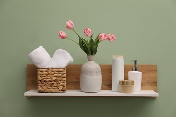 White wooden shelf with vase of pink tulips, towels and cosmetic products on light green wall