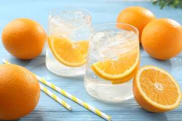 Sparkling water with orange slices in glasses, fresh fruits and straws on light blue wooden table, closeup