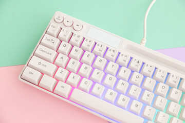 Modern computer keyboard with RGB lighting on color background, above view