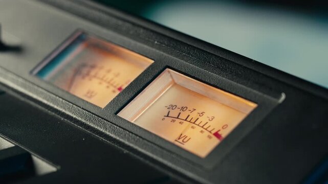 Analog dial indicator of audio signal level amplifier. Vintage arrow moves with sound level. Round classic volume indicator with yellow backlight, VU meters. Close-up of old measuring dB decibels