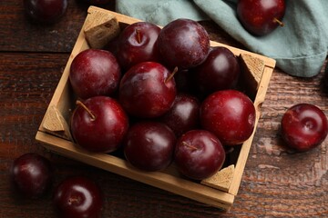 Ripe cherry plums and crate on wooden table, flat lay