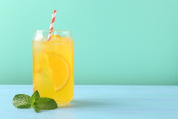 Refreshing soda water with orange slices in glass and mint on light blue wooden table against turquoise background, space for text