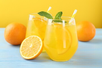 Refreshing soda water with orange slices in glasses, mint and fresh fruits on light blue wooden table, closeup