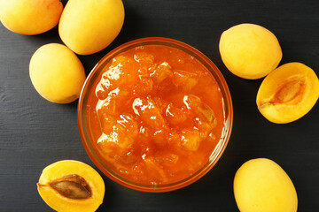 Tasty apricot jam and fresh fruits on black wooden table, flat lay