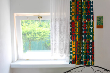 Modern bedroom window with colorful geometric patterned curtains and view of lush green garden landscape