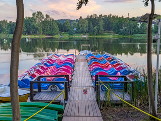 Wooden dock with colorful life jackets and kayaks overlooking serene lake at dusk