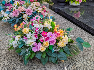 Multicolored artificial flower arrangements displayed in various containers on cemetery stone ledge creating elaborate memorial tribute collection