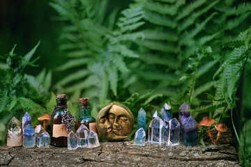 gemstone crystals, moon amulet and witch potion bottles in forest, natural background. Magic...