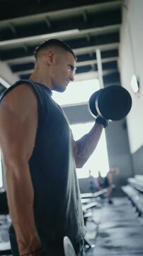 A fit man lifting dumbbells at a gym, showcasing determination and strength in a bright environment. Man Working Out with Dumbbells at Gym with Motivated Expression. Vertical