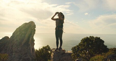 Woman, binoculars and hiking on mountain, sky and gear for sightseeing, birdwatching or adventure. Person, view and lens for landmark, outdoor and thinking with trekking on trail in summer in Spain