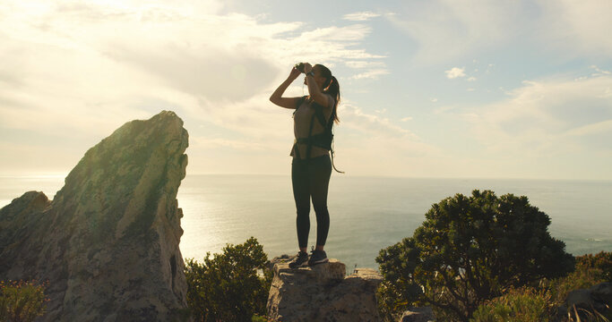 Woman, binoculars and hiking on mountain, sky and gear for sightseeing, birdwatching or adventure. Person, view and lens for landmark, outdoor and thinking with trekking on trail in summer in Spain