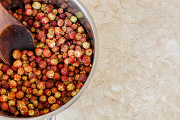 Freshly picked red wild strawberries placed in a metal bowl with a wooden spoon, on a textured surface. Berries preservation