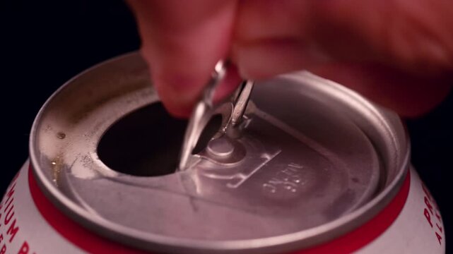 Close-up view of a hand carefully opening the pull-tab of a cold canned beer, ready for drinking. Macro shot of fingers lifting the metal pull-tab on a canned beer, moments before refreshing enjoyment