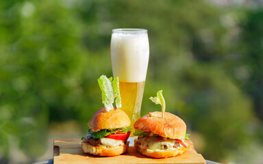 appetizing fresh made burgers with cold glass of beer  isolated on blur summer green, outdoor background 