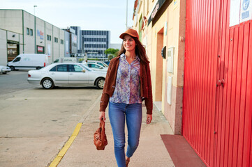 Woman walking on the sidewalk wearing casual clothes and holding a brown purse