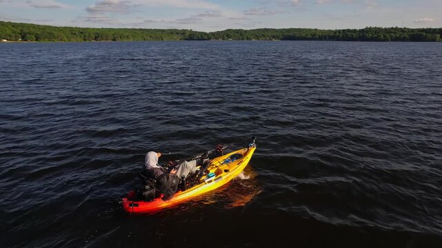 Kayak top aerial footage of yellow kayak with angler floating by in the middle of lake during golden hour sunset. Active people traveling powersport concept. Scenic view of a kayak and waves.