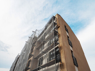 Residential apartment building during facade repair or renovation with scaffolding around it in safety mesh. Property upgrade, job increasing value of the home. Construction site.