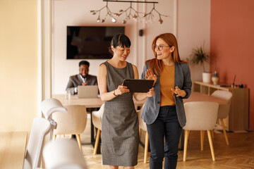 Confident female professionals discussing project while using digital tablet in modern corporate office