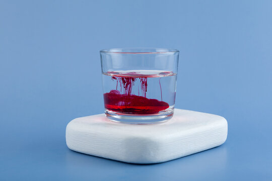 Powder of azorubine or carmoisine dissolves in water, turning it red. Glass cup with red azo dye. Food additive E122 provides stable coloring of products, high solubility and resistance to light
