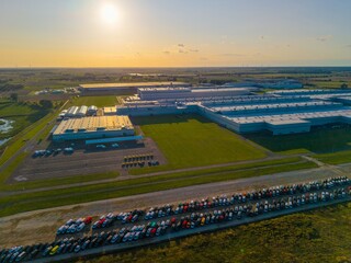 Fototapeta premium Aerial view of a car manufacturing plant at sunset, producing combustion and electric cars.